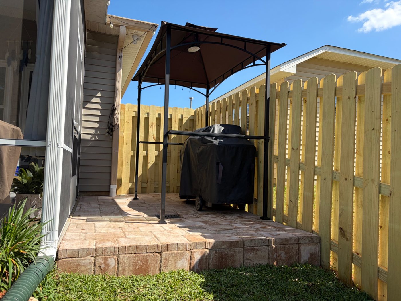 Completed paver patio and fence installation with grill canopy.